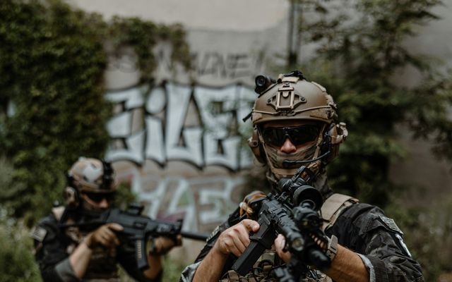 Joueurs d'airsoft équipés de gilets tactiques avancent en groupe sur un terrain extérieur