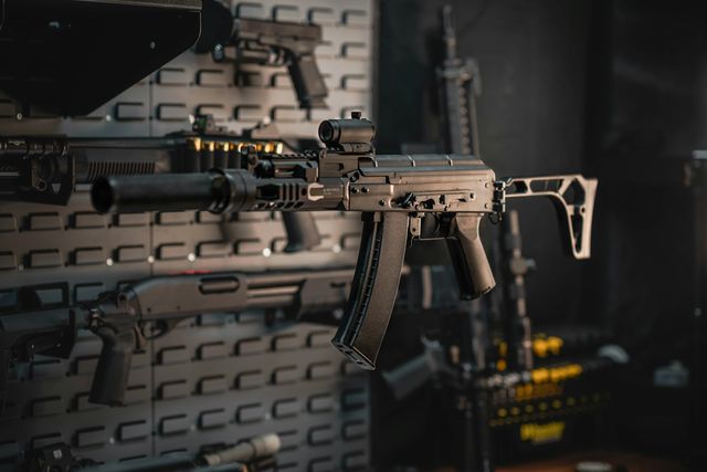 Fusil de type AK à crosse pliante et viseur point rouge, accroché sur un panneau mural
