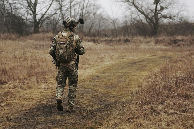 Joueur d'airsoft en tenue de terrain traversant une prairie sèche, réplique en main