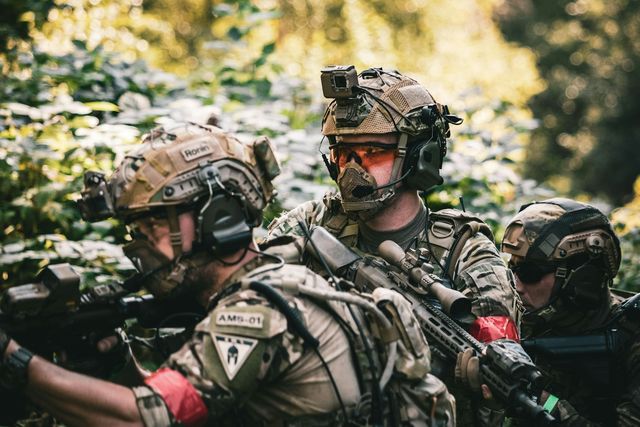 Joueur d'airsoft en tenue camouflage grise, casque et masque, de profil