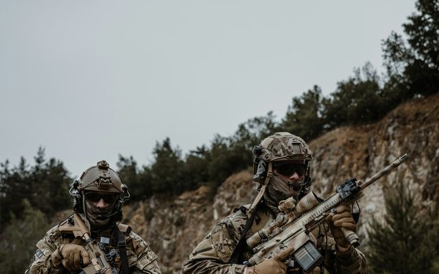Deux joueurs d'airsoft casqués et équipés progressent dans une carrière bordée d'arbres