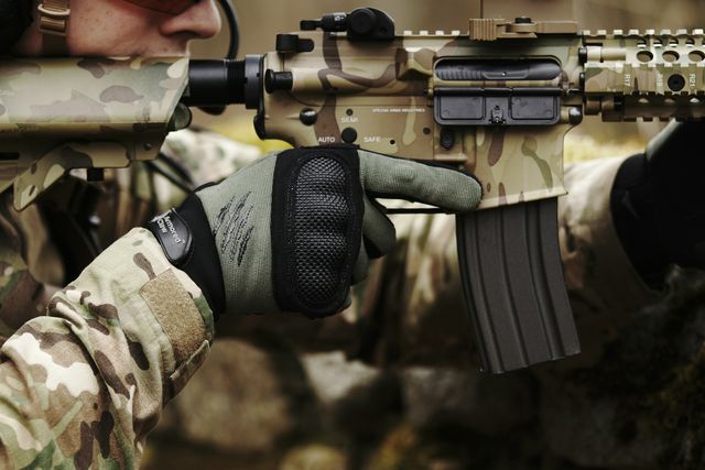 Gros plan sur un joueur d'airsoft ganté qui épaule une réplique de type M4 à garde-main long