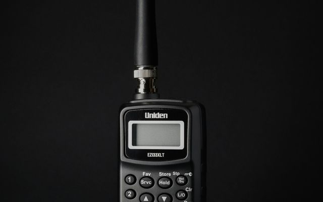 Poste radio portatif noir à antenne et écran, photographié sur fond sombre