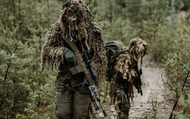 Deux joueurs d'airsoft en tenue ghillie avançant sur un chemin forestier ensoleillé