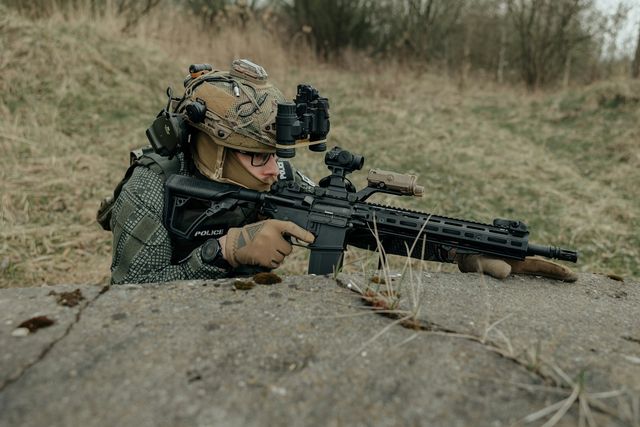 Joueur d'airsoft visant depuis un abri, derrière un élément de couverture