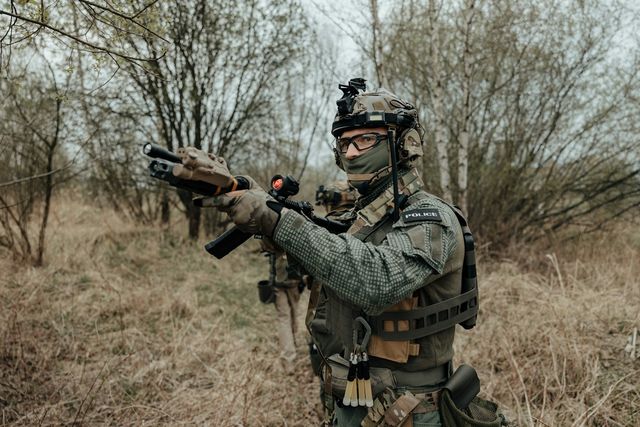 Joueur en équipement tactique en joue avec une réplique airsoft en extérieur