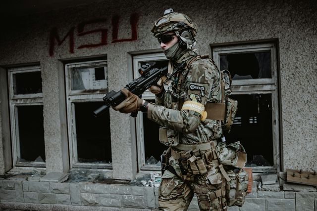 Joueur d'airsoft équipé progressant le long d'un bâtiment abandonné aux fenêtres brisées, réplique en main