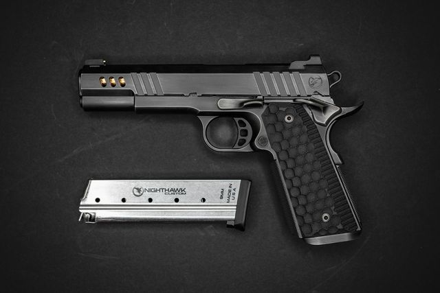 Pistolet de type 1911 à poignée noire posé sur fond sombre à côté de son chargeur