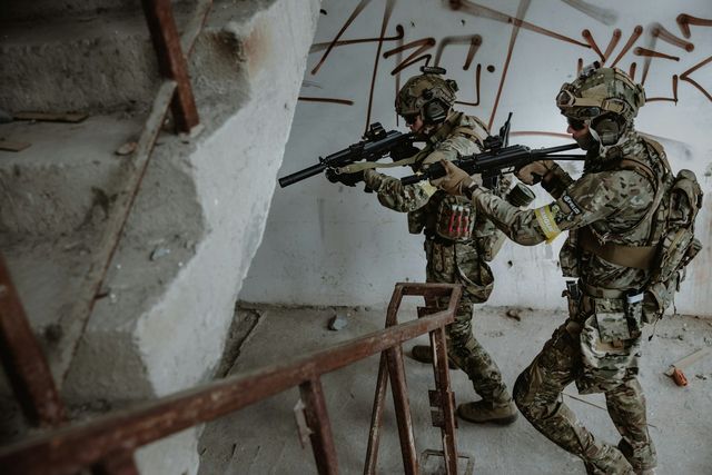Deux joueurs d'airsoft en tenue multicam progressent dans un escalier de bâtiment lors d'une partie CQB