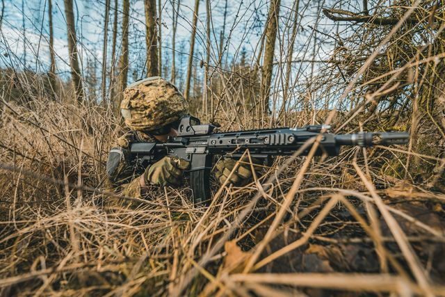 Réplique airsoft type fusil d'assaut posée sur un tapis de feuilles mortes en forêt