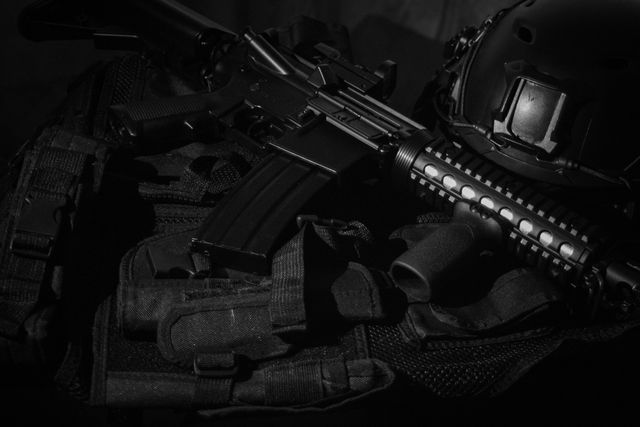 Réplique de fusil noire et équipement posés sur un tissu sombre, en lumière rasante