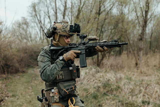 Joueur d'airsoft en tenue tactique avec sa réplique dans un environnement boisé