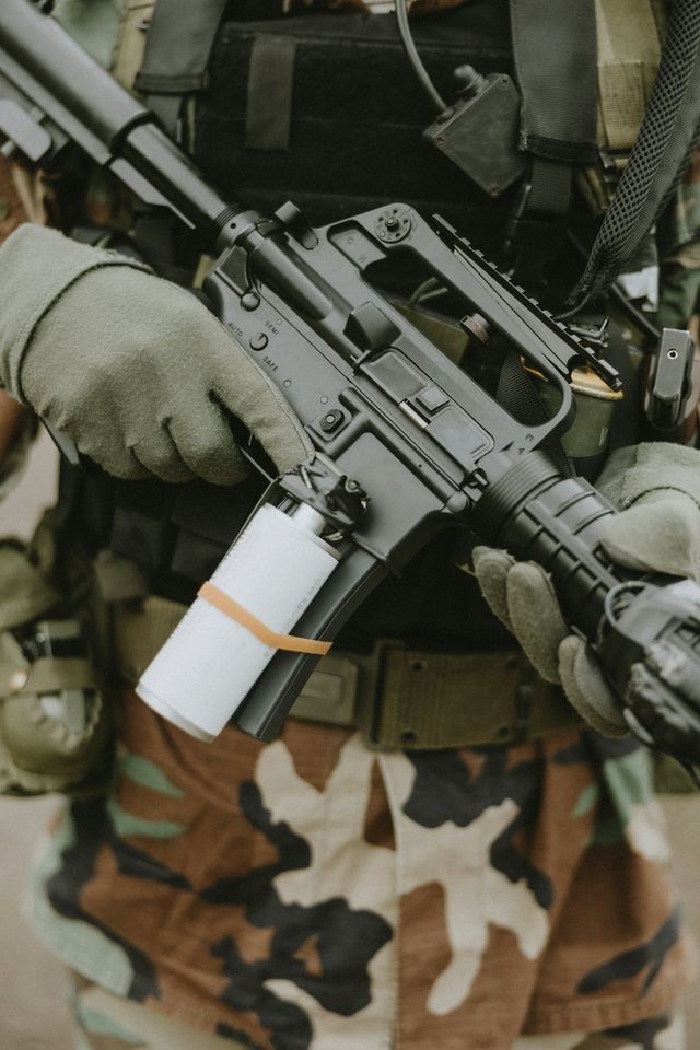 Joueur d'airsoft en tenue camouflage tenant une réplique type fusil d'assaut, en sous-bois