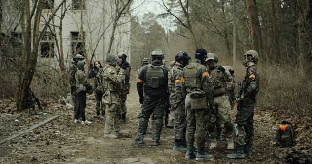 Groupe de joueurs d'airsoft équipés réunis pour un briefing au milieu d'un bois, devant un bâtiment abandonné