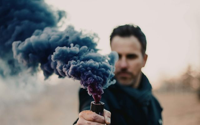 Homme tenant à bout de bras un fumigène qui dégage une épaisse fumée bleue