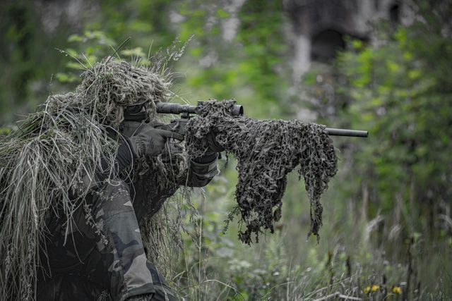 Tireur en tenue ghillie épaulant une réplique à lunette au milieu de la végétation